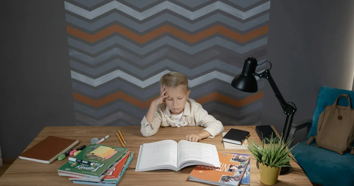 A young boy sitting at a desk, focused on homework with school supplies around him, representing concentration and productivity.