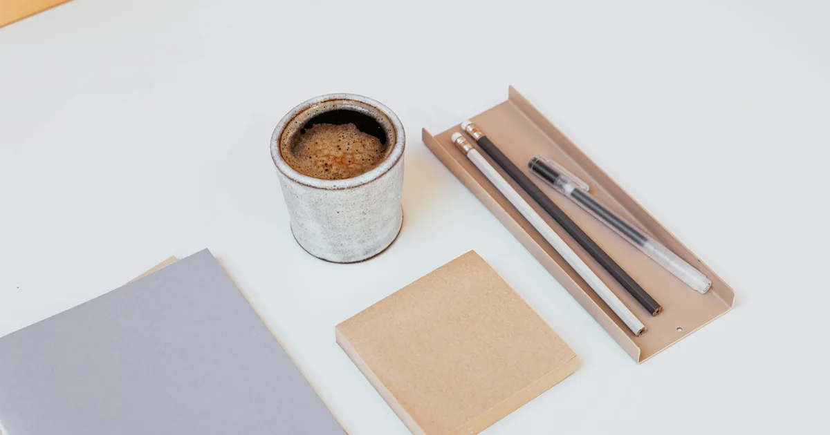 A minimalist desk setup with coffee, notebooks, and writing tools on a clean white surface, promoting focus and productivity.